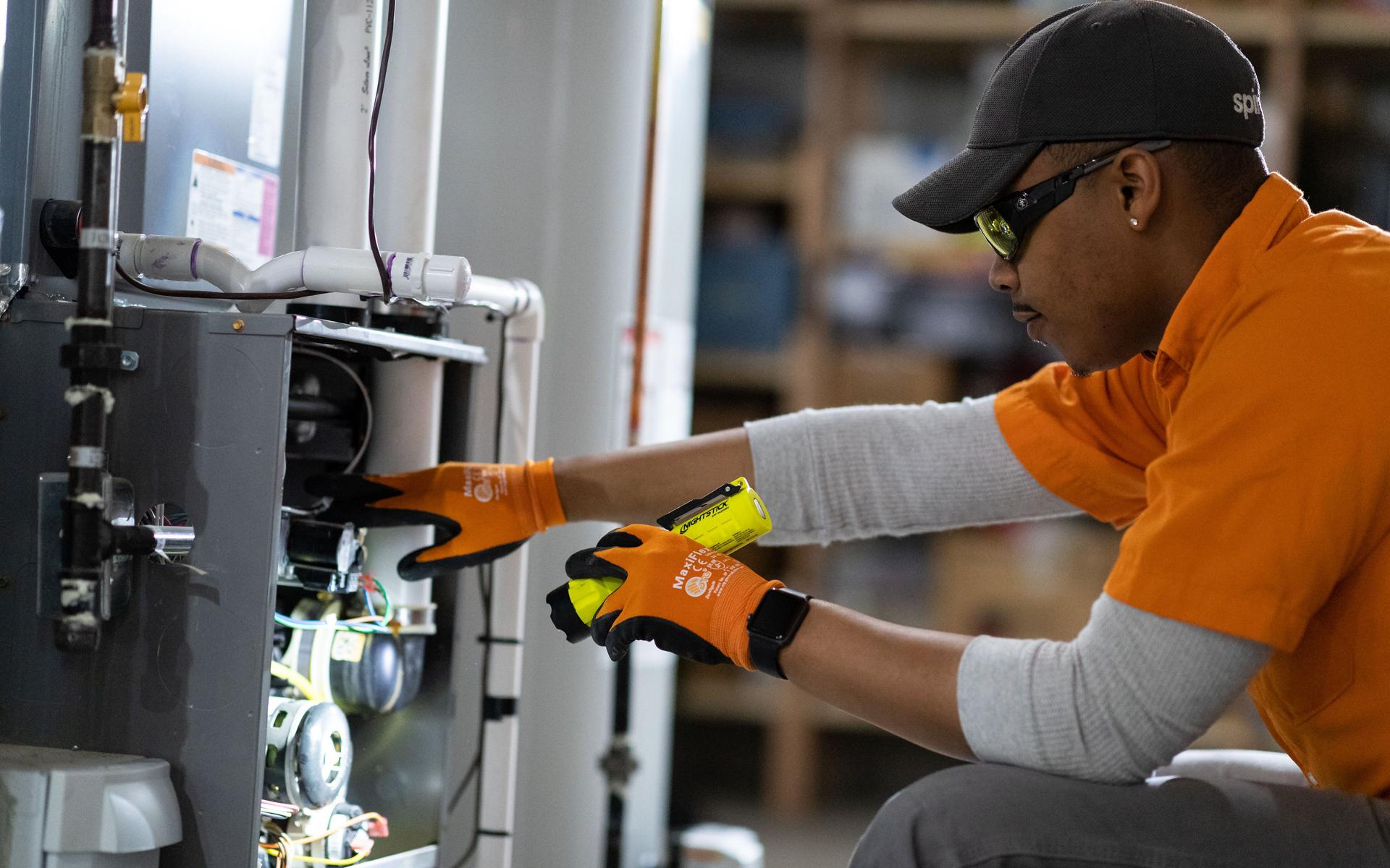 Image of Spire technician wearing an orange uniform shirt and working on a furnace. 